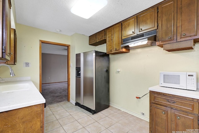 kitchen featuring stainless steel refrigerator with ice dispenser, light tile patterned flooring, sink, and a textured ceiling