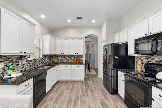 kitchen with white cabinetry, wood-type flooring, black appliances, dark stone counters, and backsplash