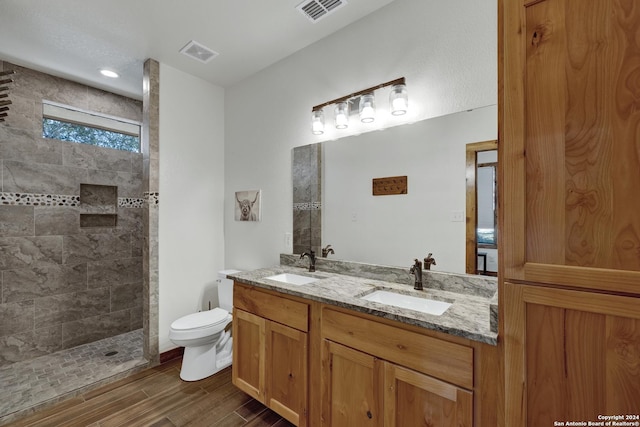 bathroom with wood-type flooring, toilet, vanity, and a tile shower