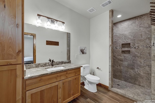 bathroom featuring hardwood / wood-style flooring, vanity, toilet, and a tile shower