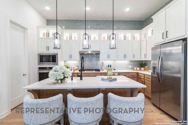 kitchen with pendant lighting, white cabinetry, stainless steel appliances, and a center island with sink