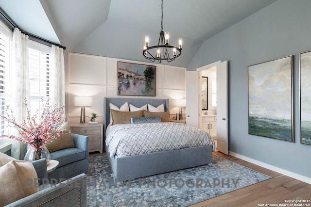 bedroom featuring vaulted ceiling, wood-type flooring, a notable chandelier, and ensuite bath