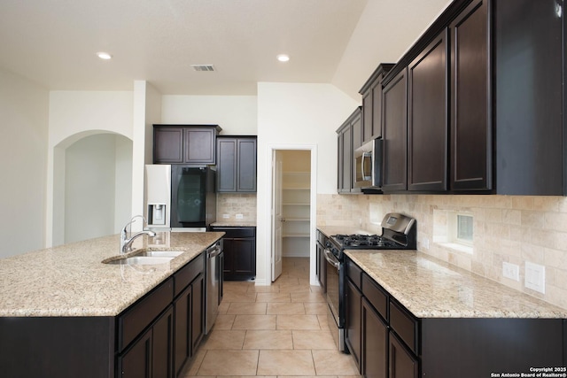 kitchen featuring an island with sink, sink, decorative backsplash, stainless steel appliances, and light stone countertops