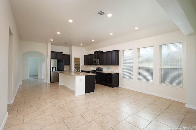 kitchen with light tile patterned flooring, backsplash, a kitchen island with sink, light stone counters, and stainless steel appliances