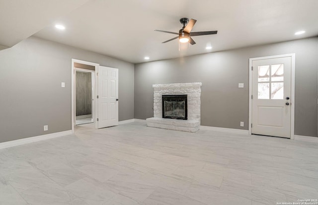 unfurnished living room featuring ceiling fan and a stone fireplace