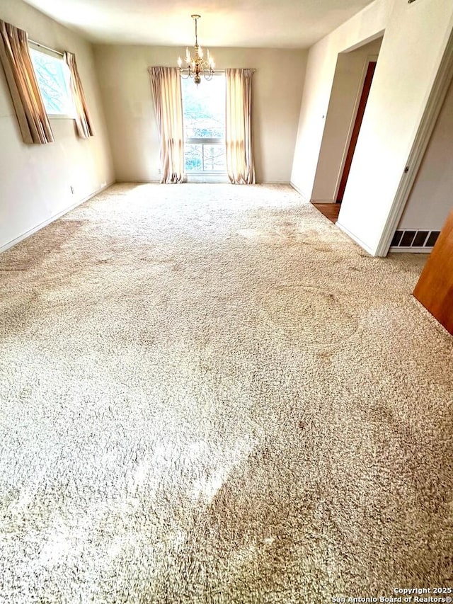 carpeted spare room with plenty of natural light and a notable chandelier