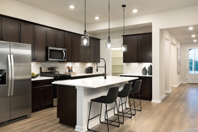 kitchen with stainless steel appliances, a kitchen island with sink, dark brown cabinetry, and decorative light fixtures