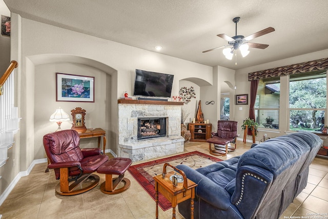 living room with ceiling fan, a fireplace, a textured ceiling, and light tile patterned floors