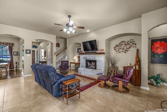 living room with light tile patterned flooring, ceiling fan, and a stone fireplace