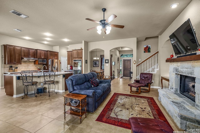 tiled living room featuring sink, a stone fireplace, a textured ceiling, and ceiling fan