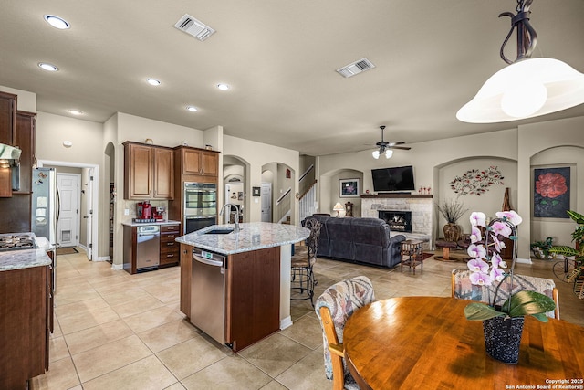 kitchen featuring sink, a fireplace, light stone countertops, an island with sink, and stainless steel dishwasher