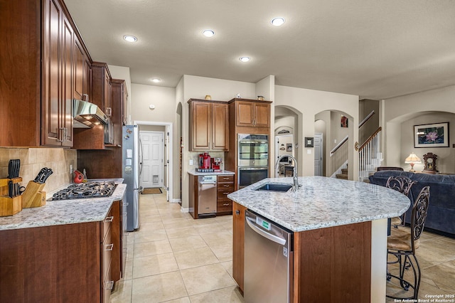 kitchen featuring sink, light stone counters, appliances with stainless steel finishes, a kitchen island with sink, and backsplash