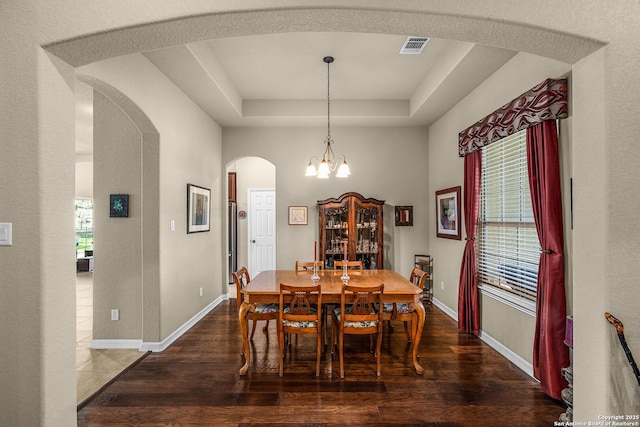 dining room featuring a notable chandelier, a tray ceiling, and dark wood-type flooring