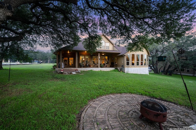 back house at dusk with a sunroom, a patio, a fire pit, and a lawn