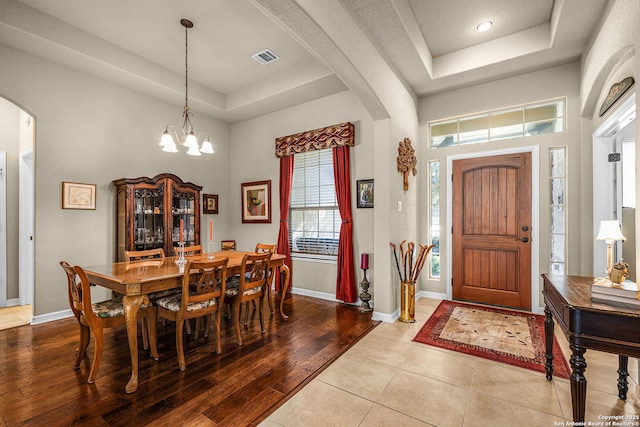 foyer featuring an inviting chandelier, a towering ceiling, a raised ceiling, and light hardwood / wood-style floors