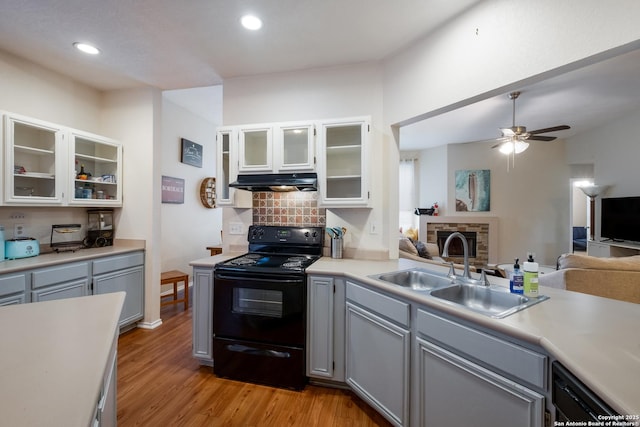 kitchen featuring sink, gray cabinetry, black appliances, a stone fireplace, and light wood-type flooring