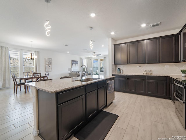 kitchen with sink, dark brown cabinets, hanging light fixtures, a center island with sink, and plenty of natural light