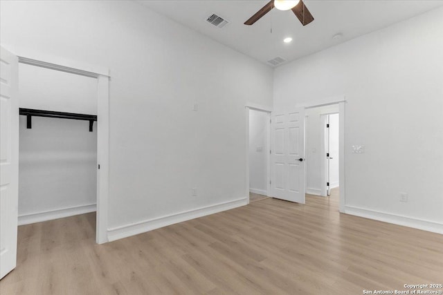 empty room with ceiling fan, light hardwood / wood-style flooring, and a towering ceiling