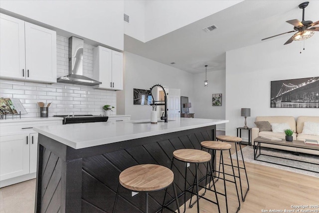 kitchen featuring wall chimney range hood, sink, white cabinets, and a spacious island