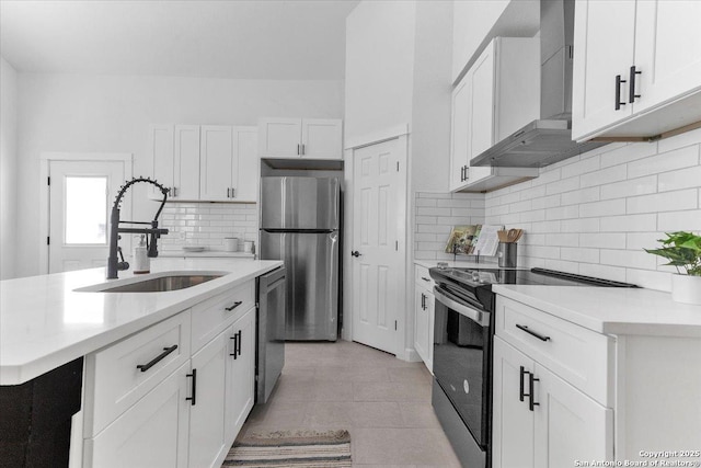 kitchen featuring wall chimney range hood, sink, appliances with stainless steel finishes, white cabinetry, and a center island with sink