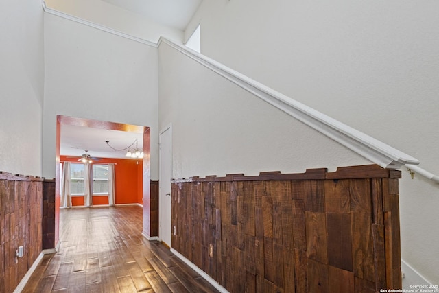 staircase with a towering ceiling, wood-type flooring, ceiling fan, and wood walls