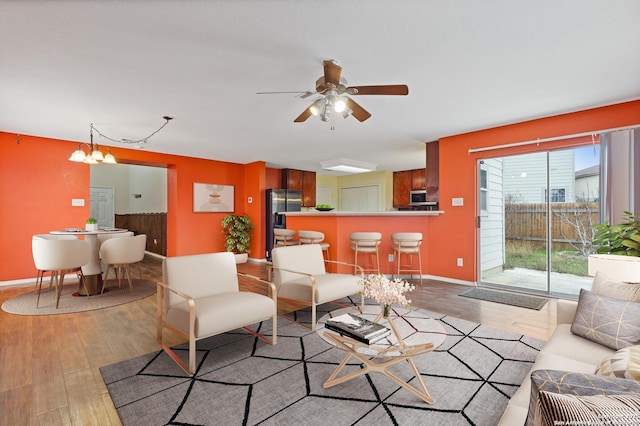 living room with ceiling fan with notable chandelier and light wood-type flooring