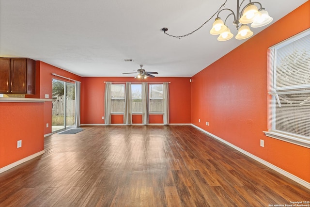 unfurnished living room featuring ceiling fan with notable chandelier, a wealth of natural light, and dark hardwood / wood-style flooring