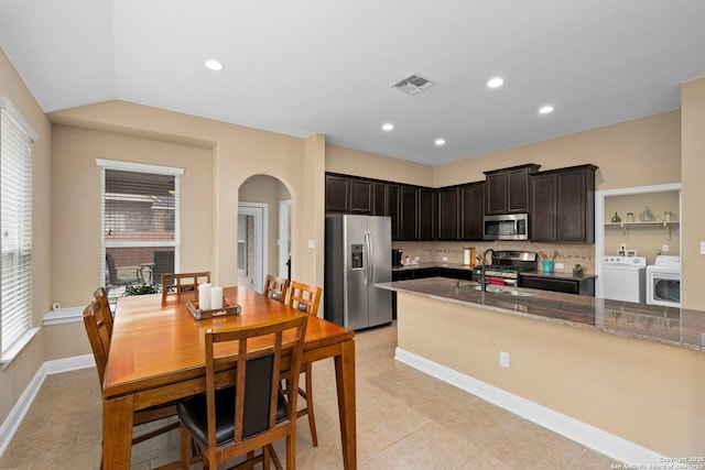 kitchen with appliances with stainless steel finishes, dark stone countertops, dark brown cabinetry, washer and dryer, and decorative backsplash