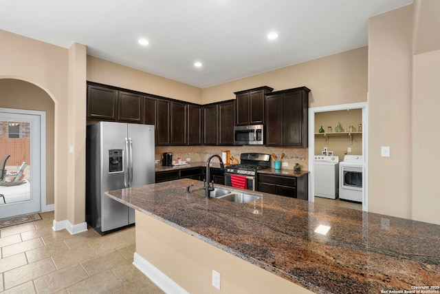 kitchen featuring dark brown cabinetry, sink, dark stone countertops, appliances with stainless steel finishes, and washer and clothes dryer