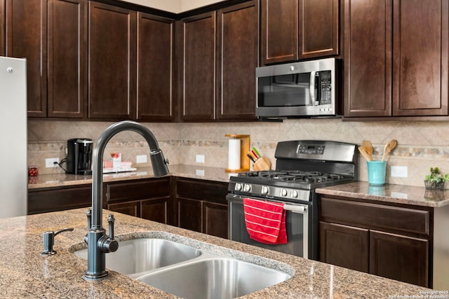 kitchen featuring dark brown cabinetry, sink, tasteful backsplash, appliances with stainless steel finishes, and light stone countertops