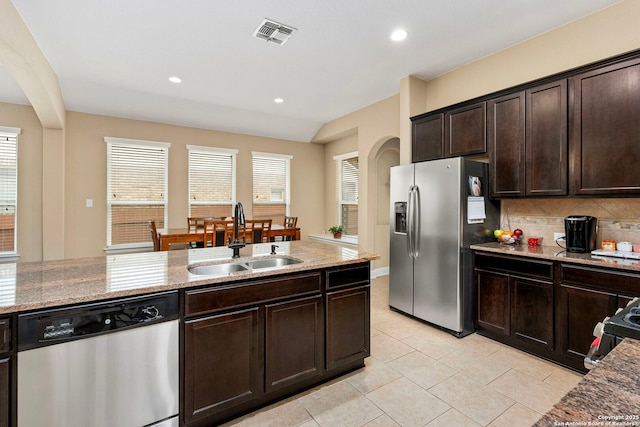 kitchen with sink, dark brown cabinets, stainless steel appliances, light stone counters, and decorative backsplash