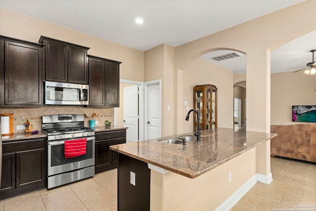 kitchen featuring sink, stainless steel appliances, tasteful backsplash, light stone countertops, and an island with sink