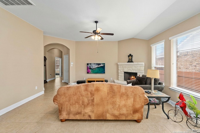 living room featuring vaulted ceiling, a stone fireplace, light tile patterned floors, and ceiling fan