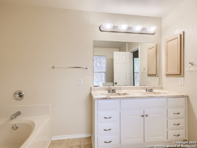 bathroom featuring tile patterned flooring, vanity, a bath, and a textured ceiling