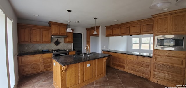 kitchen with sink, stainless steel appliances, an island with sink, dark tile patterned flooring, and decorative light fixtures