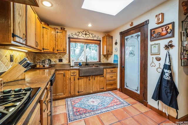 kitchen with sink, gas stovetop, a skylight, light tile patterned floors, and backsplash