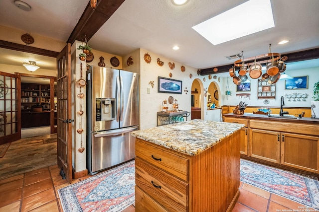 kitchen with stainless steel refrigerator with ice dispenser, light tile patterned flooring, sink, a kitchen island, and beamed ceiling