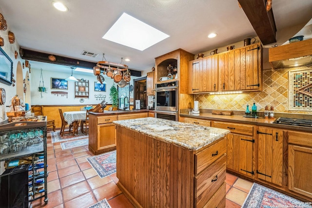 kitchen featuring a kitchen island, a skylight, backsplash, kitchen peninsula, and stainless steel appliances