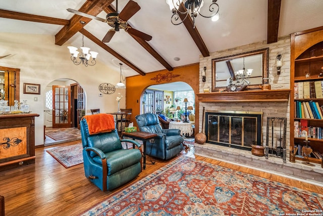 living room with hardwood / wood-style floors, ceiling fan with notable chandelier, a fireplace, and lofted ceiling with beams