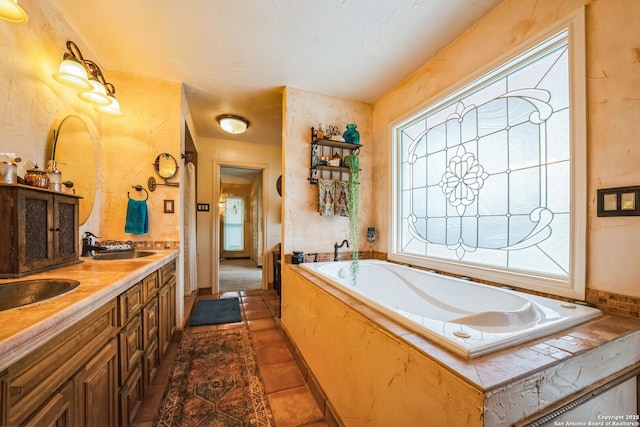 bathroom with a relaxing tiled tub, vanity, and tile patterned floors