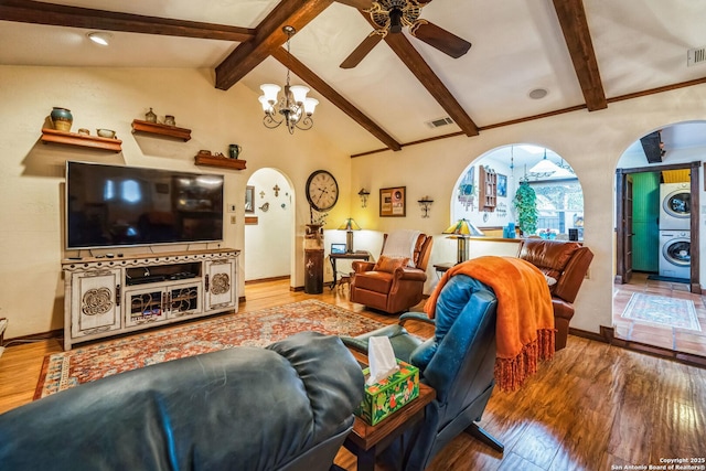 living room featuring stacked washer and dryer, wood-type flooring, beam ceiling, and ceiling fan with notable chandelier