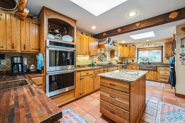 kitchen featuring sink, a skylight, a kitchen island, stainless steel appliances, and backsplash