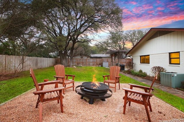 patio terrace at dusk featuring central AC, a yard, and a fire pit