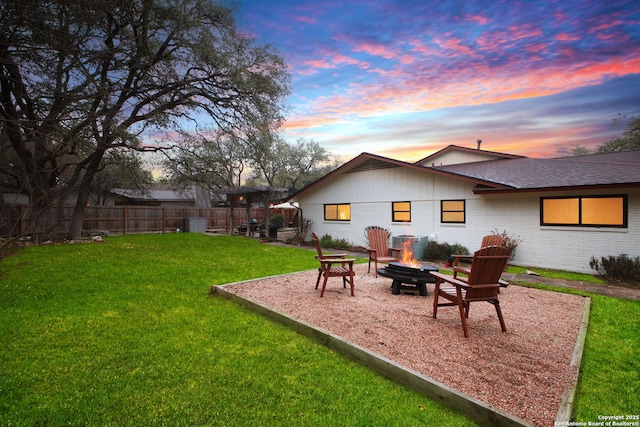 back house at dusk featuring an outdoor fire pit and a lawn