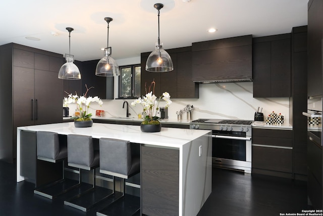 kitchen with pendant lighting, wall chimney exhaust hood, a kitchen island, and high end stove