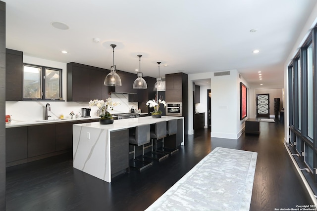 kitchen with sink, a breakfast bar area, hanging light fixtures, a center island, and stainless steel oven