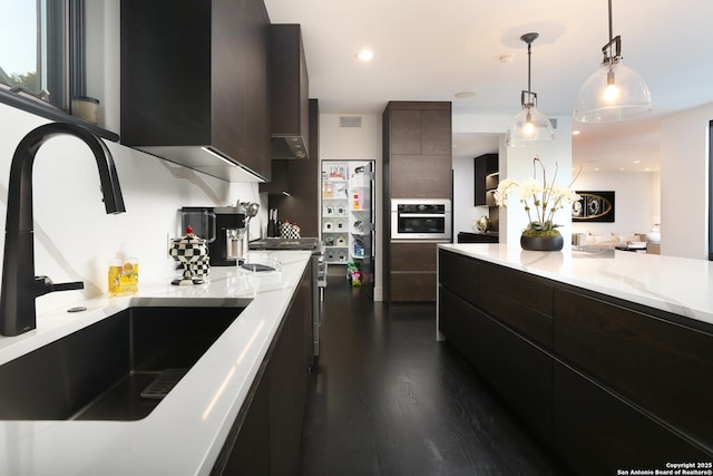 kitchen with sink, dark hardwood / wood-style floors, dark brown cabinetry, decorative light fixtures, and stainless steel oven