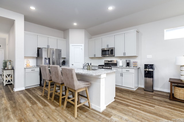 kitchen with light stone counters, appliances with stainless steel finishes, a kitchen breakfast bar, an island with sink, and white cabinets