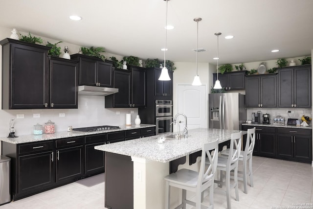 kitchen featuring sink, appliances with stainless steel finishes, a center island with sink, a kitchen bar, and decorative light fixtures