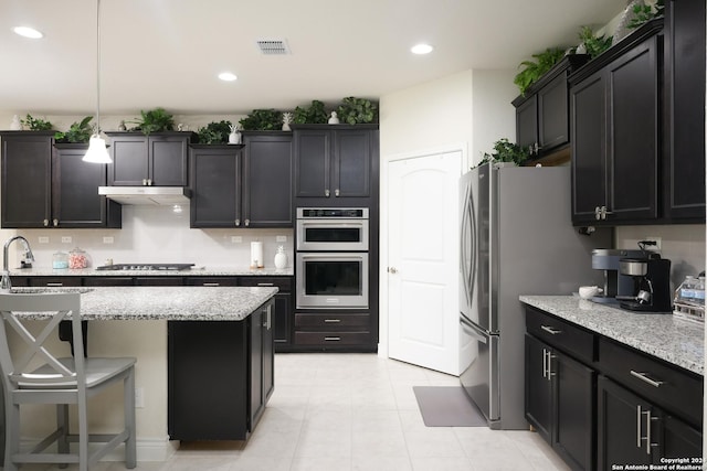 kitchen with light stone counters, hanging light fixtures, a center island, and appliances with stainless steel finishes